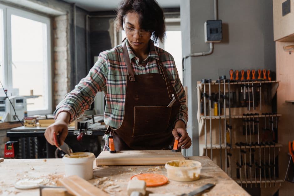 Woodworker spreading wood glue on a plank at a workbench with clamps ready alongside