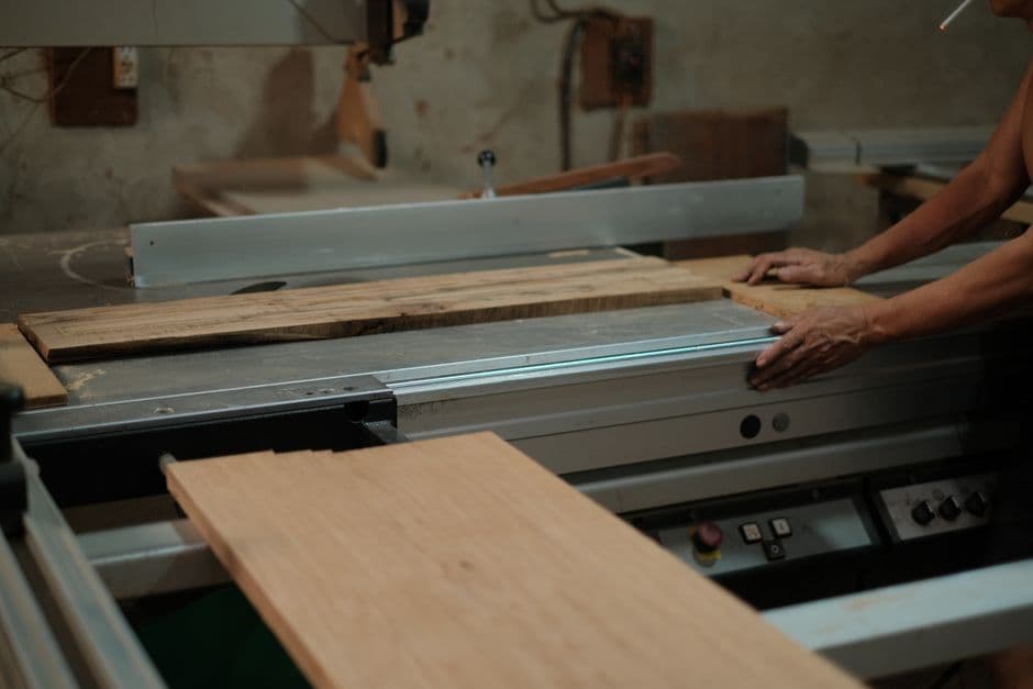 A person guiding a wide wooden panel across a table saw in a workshop