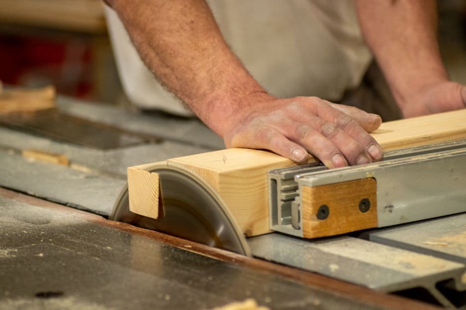 Hands feeding a board through a table saw blade, sawdust visible in the cut