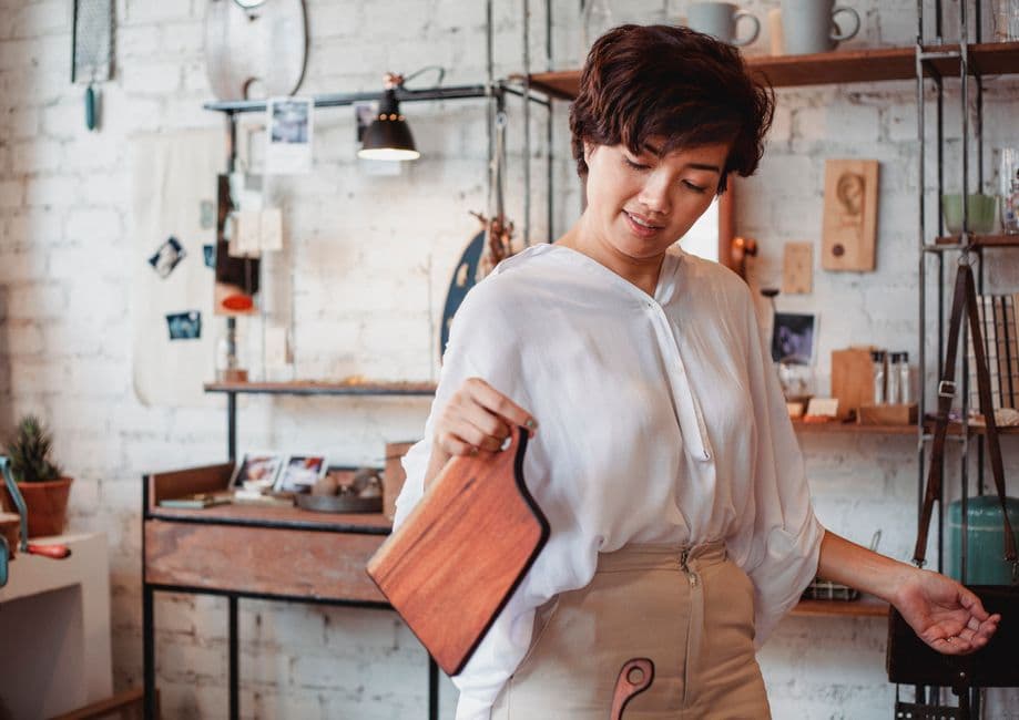 Woman holding a wooden cutting board in a small craft store with brick walls