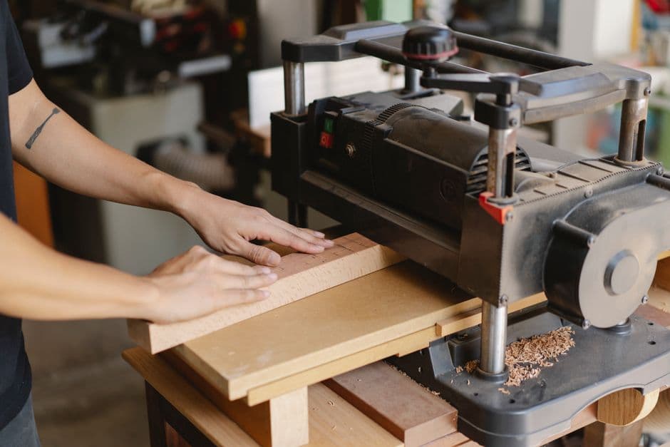 Woodworker feeding a wide board into a benchtop thickness planer in a daylit workshop