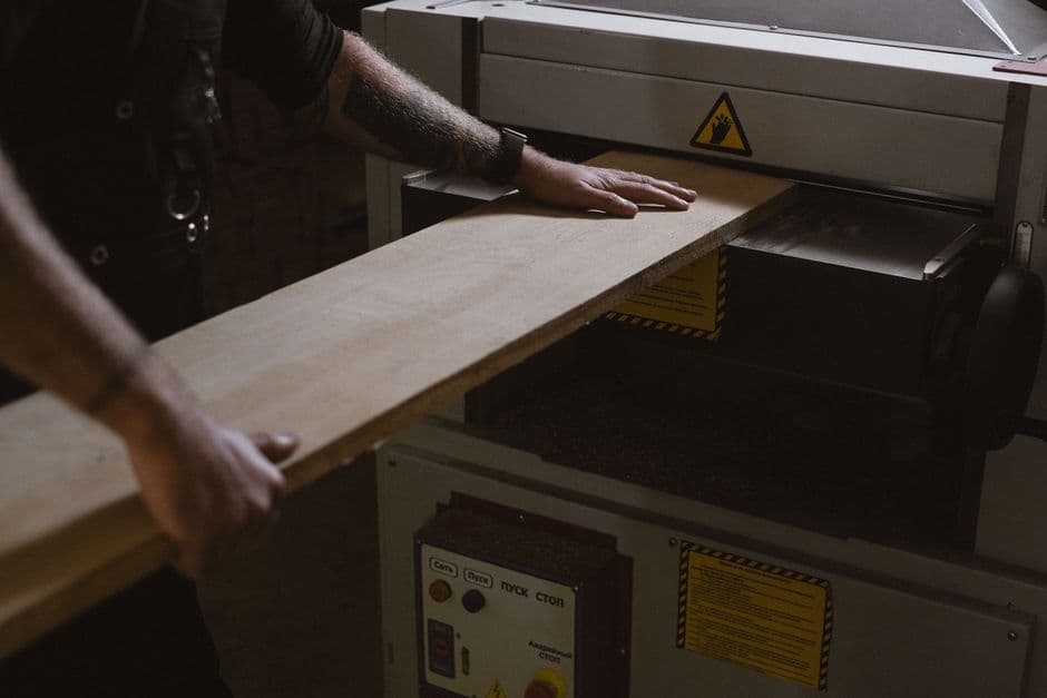 A woodworker feeding a board through a thickness planer in a workshop