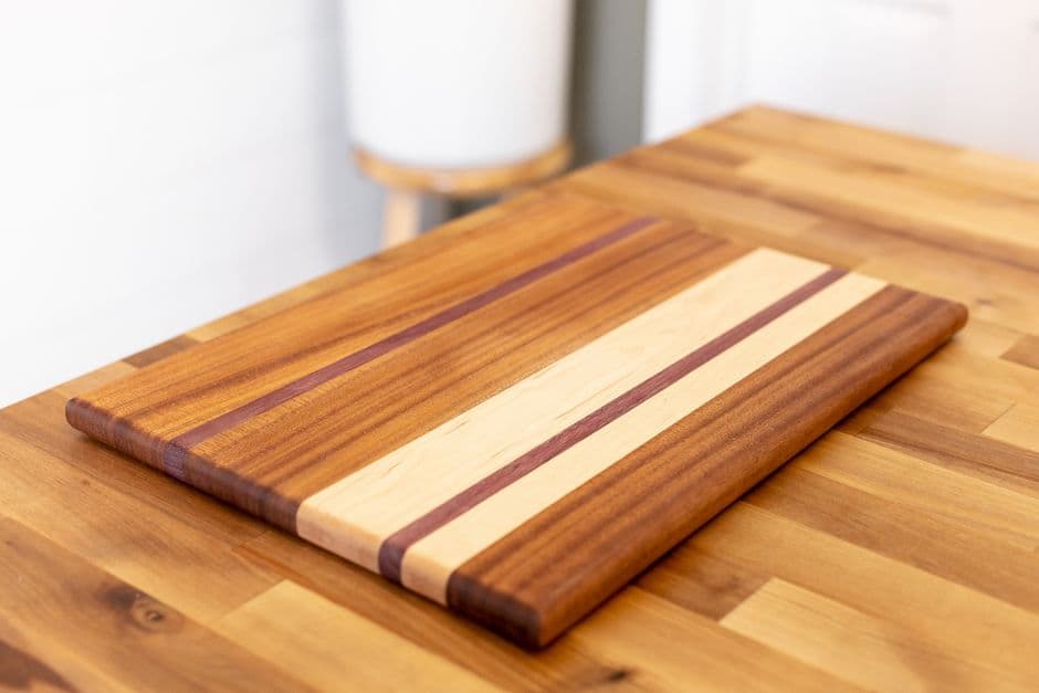 A finished striped hardwood cutting board resting on a butcher block counter