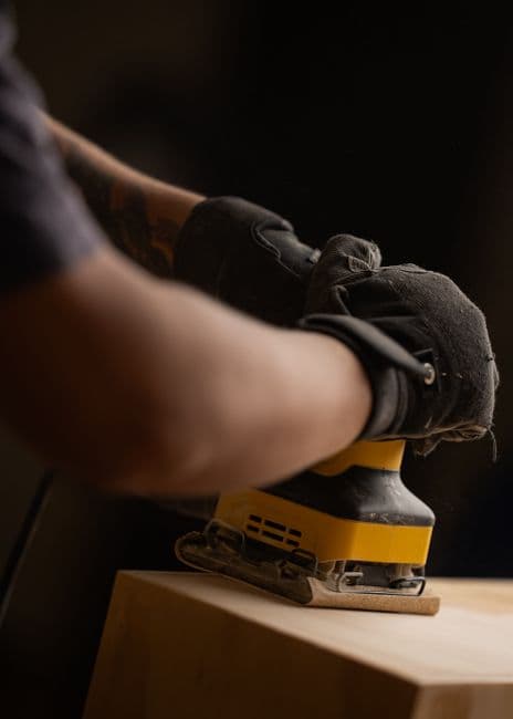A woodworker sanding a block of pale hardwood with a power sander